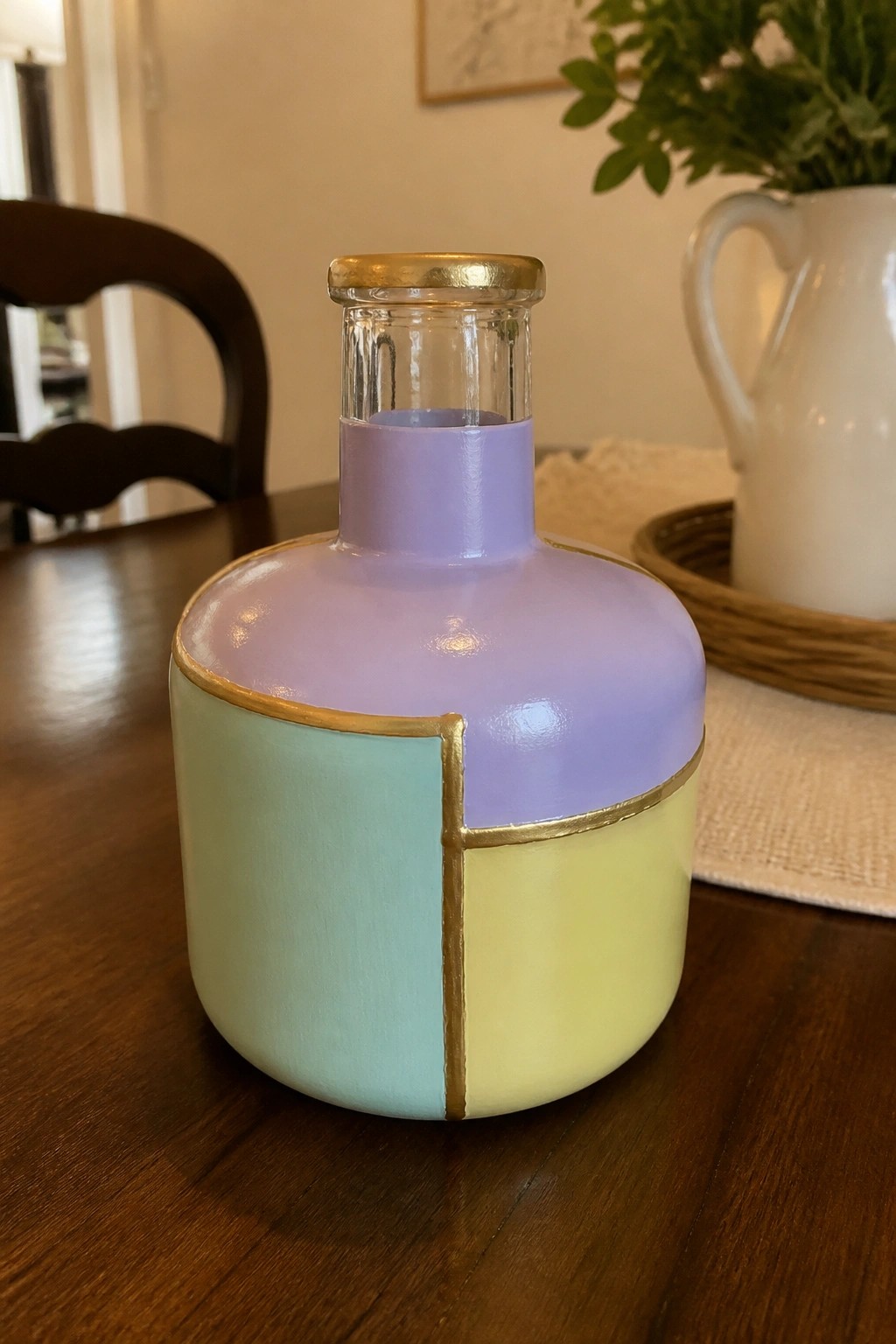 Pastel-painted glass bottle with mint, yellow, lavender sections and gold lines on table.