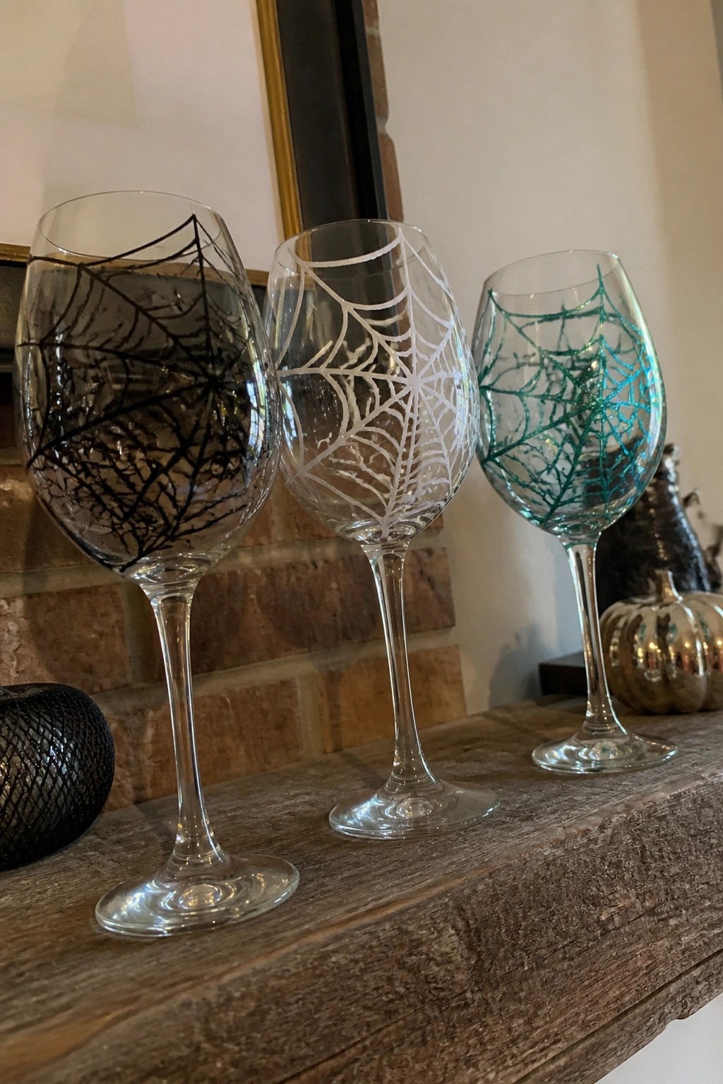 Three wine glasses with black, white, and teal spiderweb designs on wooden shelf