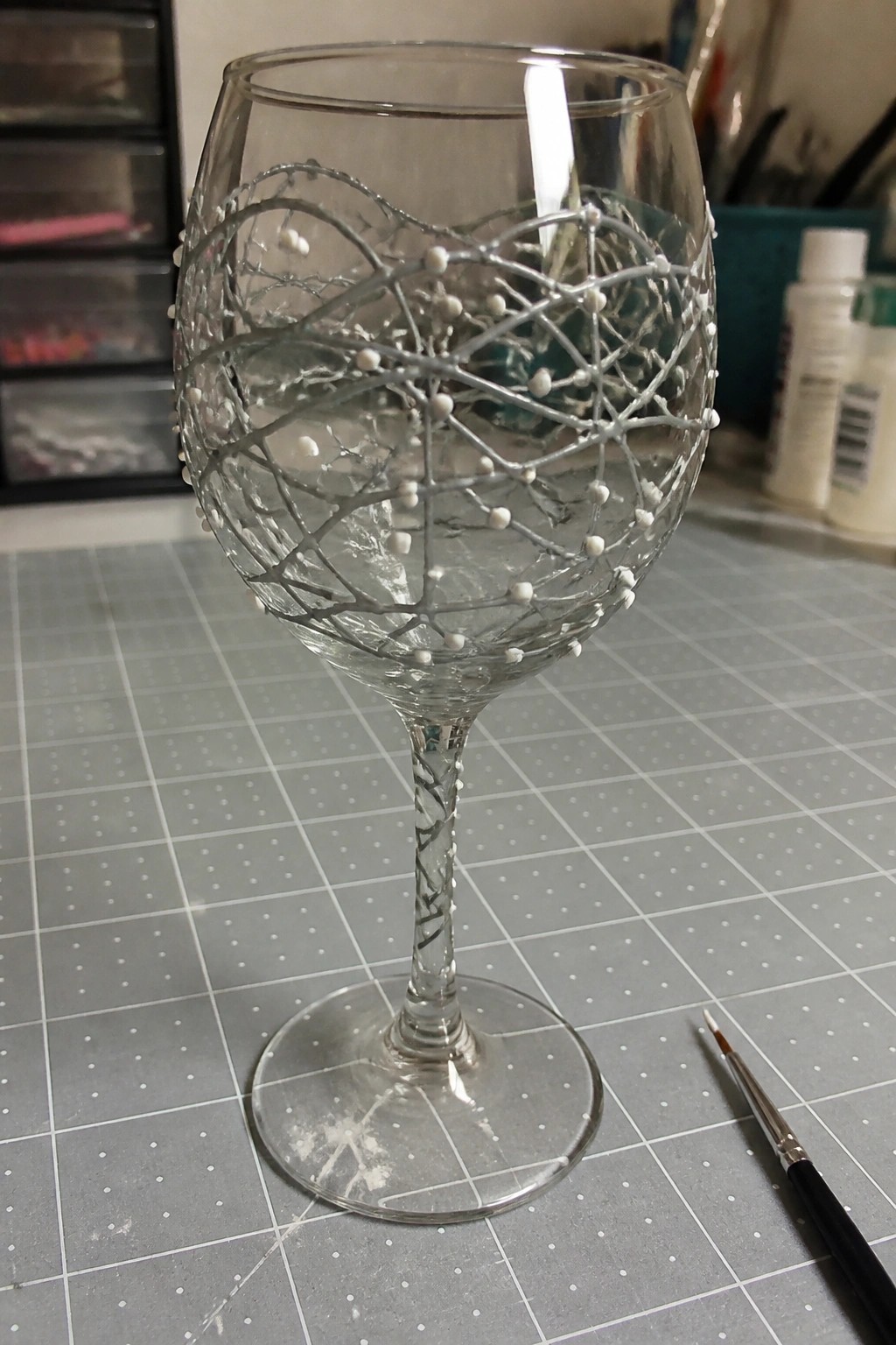 Decorated wine glass with gray branching design and white dots on gridded mat