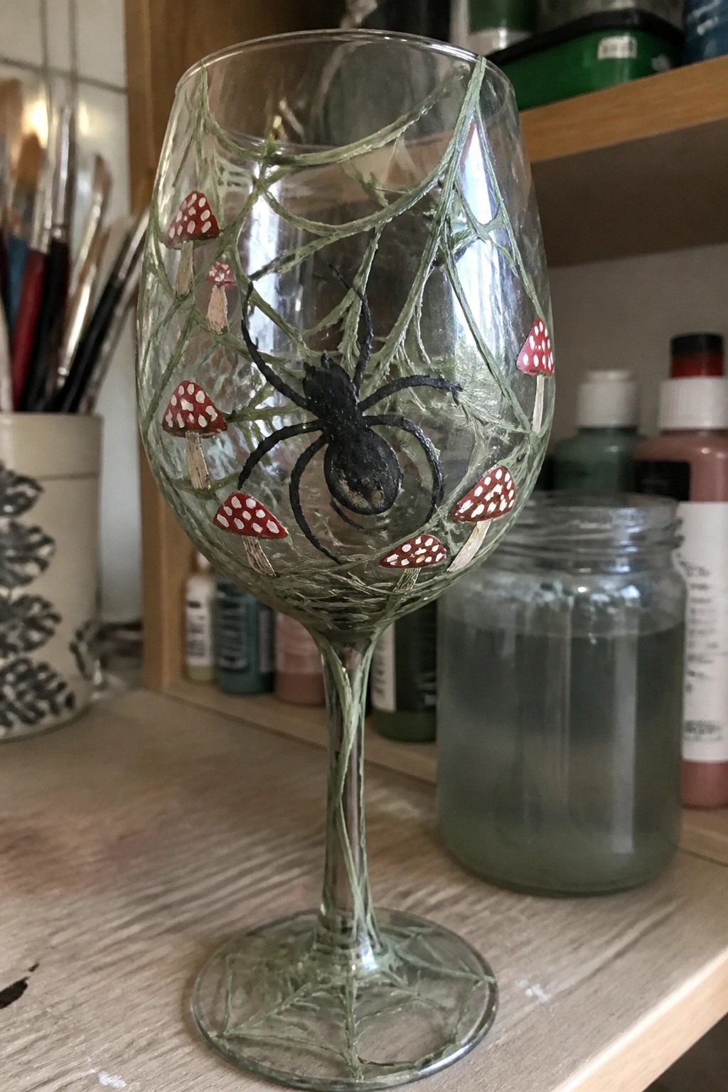 Hand-painted wine glass with black spider, green web, and red mushrooms