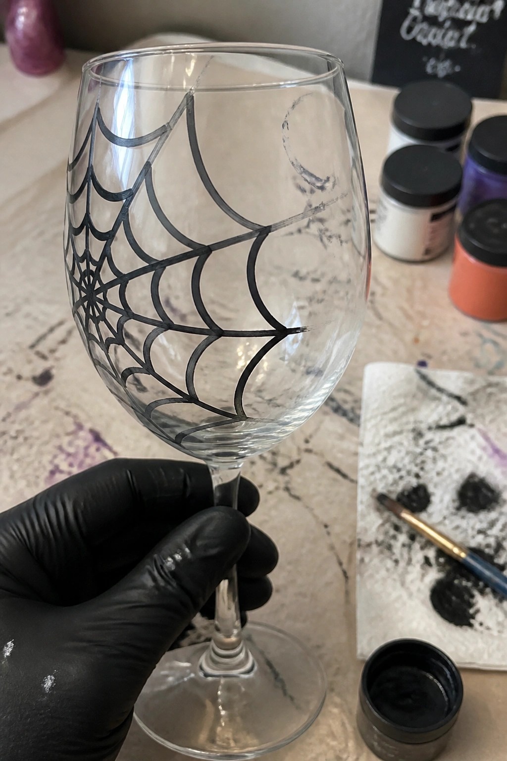 Black-gloved hand holding wine glass with black spiderweb paint design