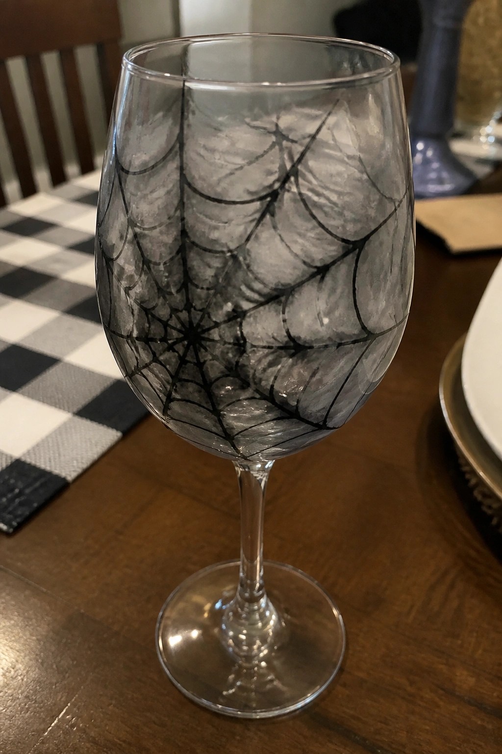 Clear wine glass with black spiderweb design on wooden table with checkered mat