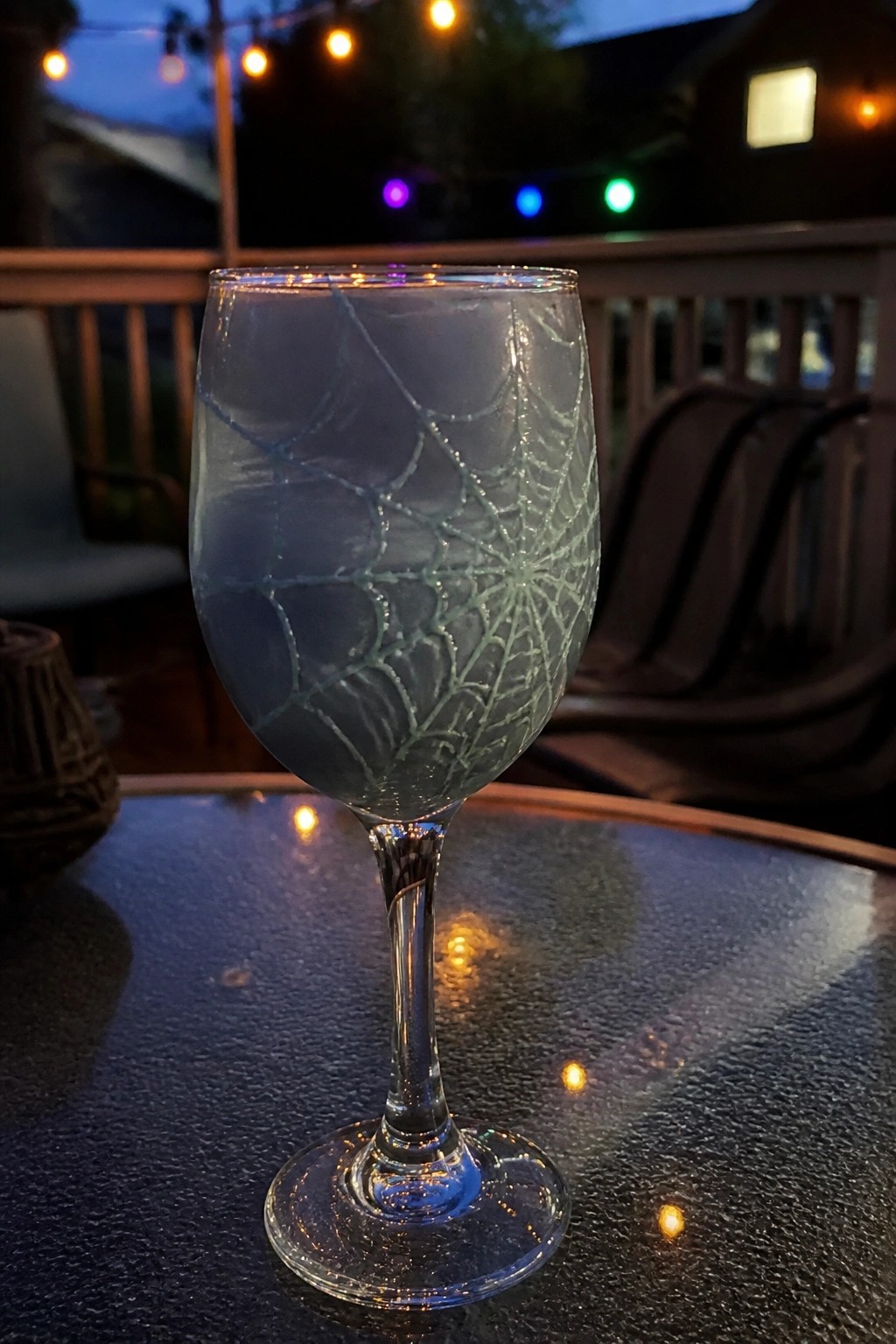 Spiderweb-etched wine glass on patio table under string lights at dusk