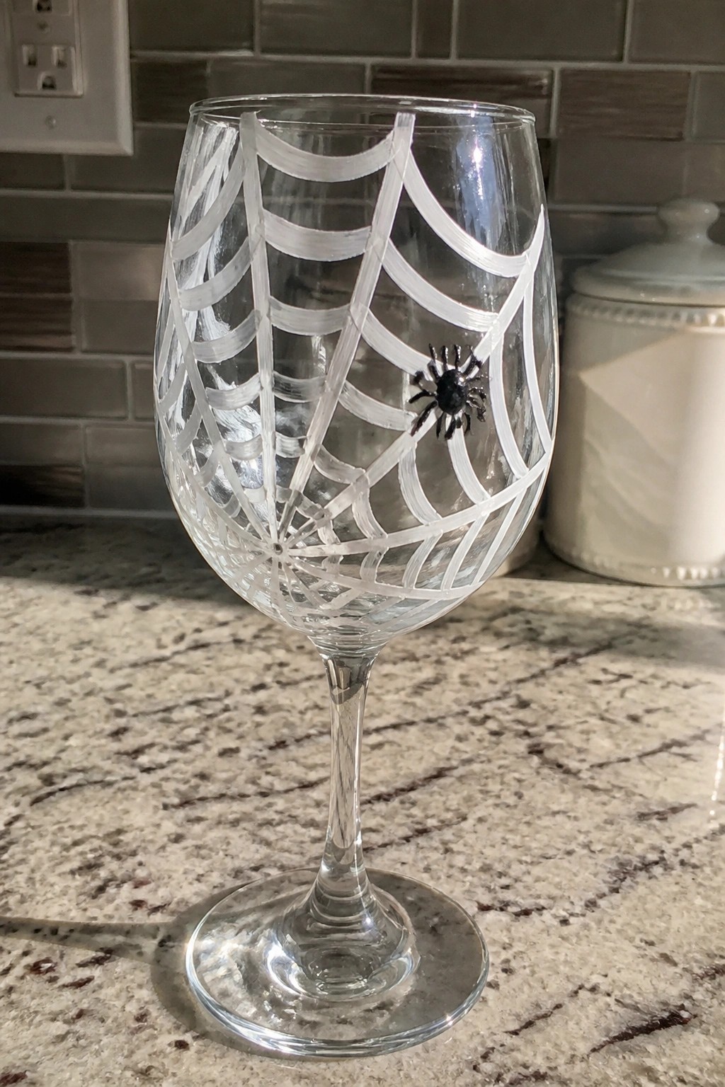 Wine glass with white spiderweb design and black spider on kitchen counter