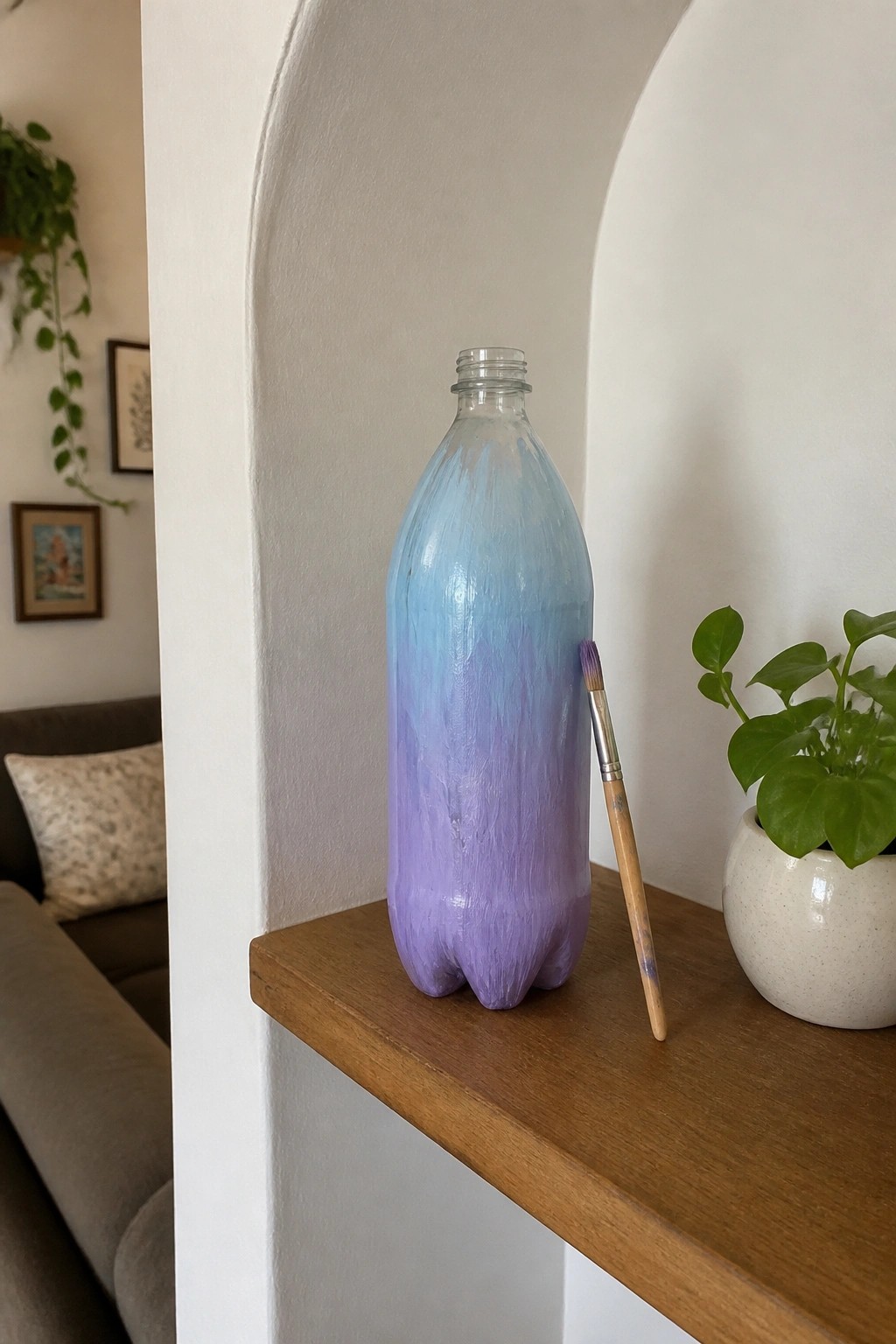 Painted blue-to-purple bottle with brush on wooden shelf beside potted plant