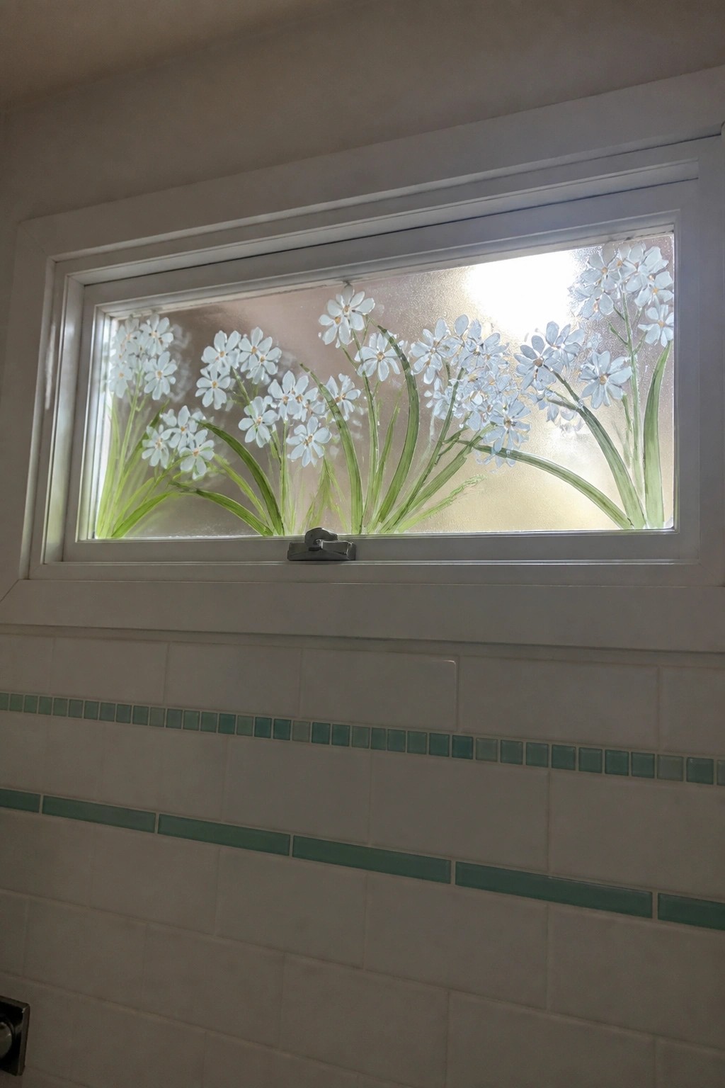Frosted window with white flowers and green stems above white tiles with green accents