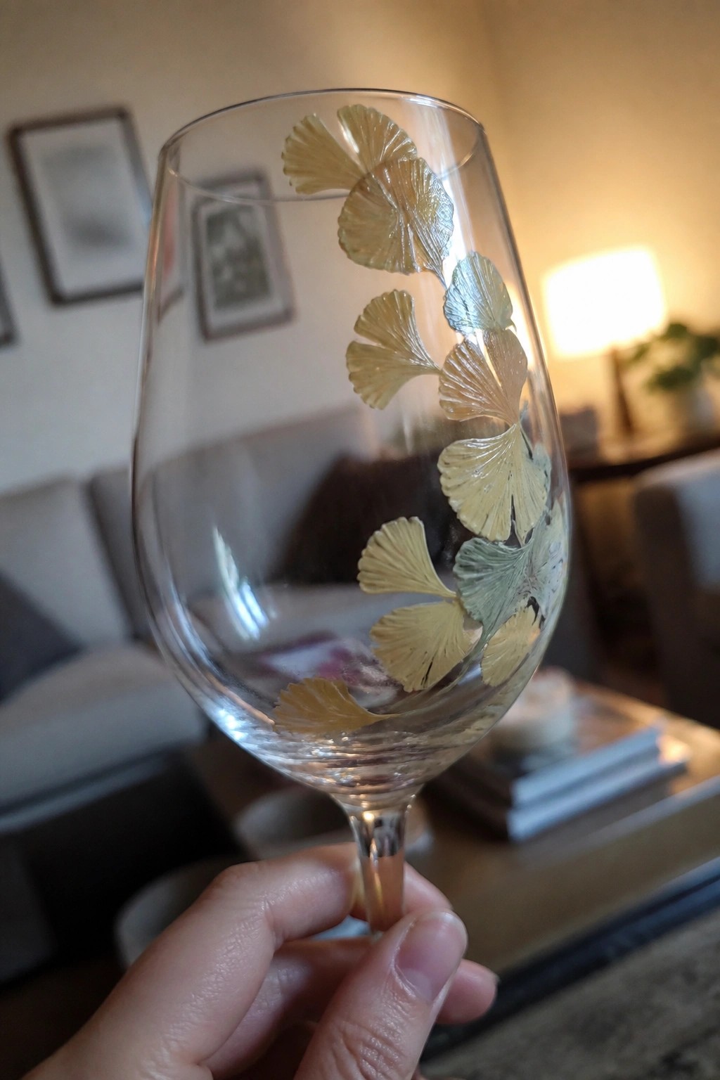 Hand holding wine glass with gold and green ginkgo leaf designs.