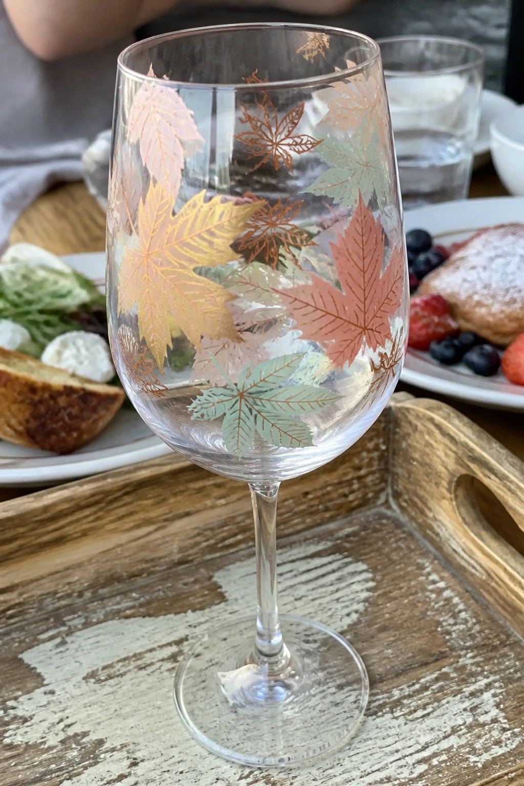 Wine glass with colorful autumn maple leaves on rustic wooden tray