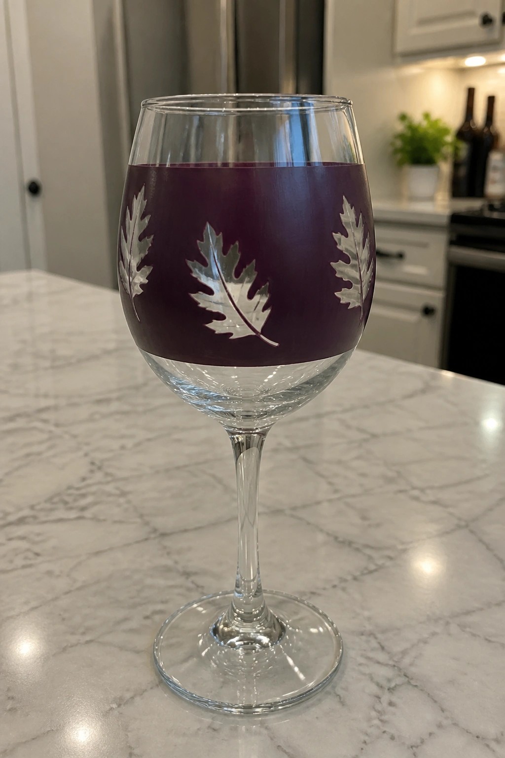 Purple-banded wine glass with silver leaf etchings filled with wine on marble counter