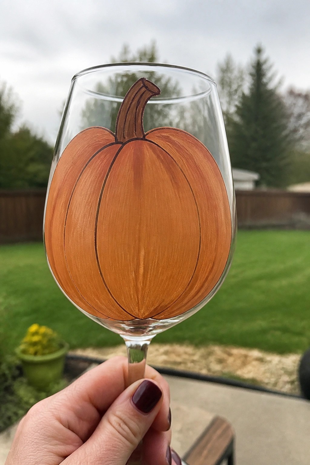 Hand holding wine glass painted with large orange pumpkin outdoors.