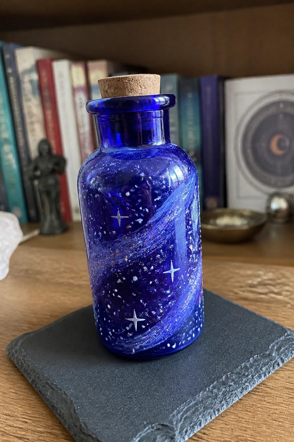 Blue glass bottle with starry swirls and white stars, corked on dark slate coaster.