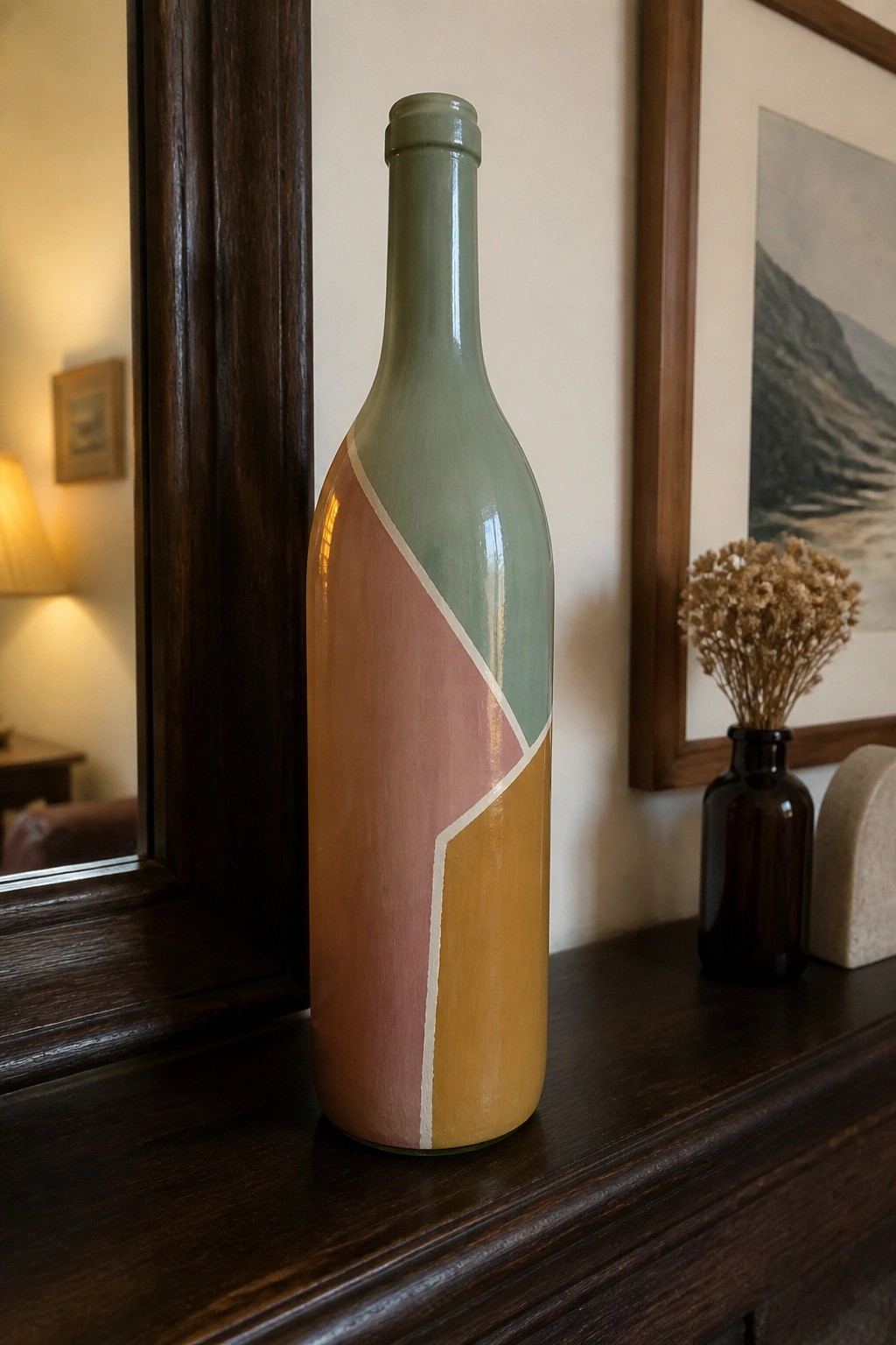 Painted bottle with sage green, pink, and mustard yellow geometric sections on wood