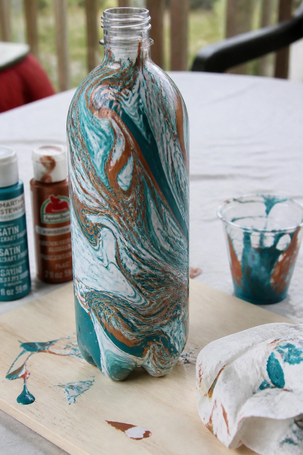 Marbled teal brown and white painted bottle on wooden board with paint supplies