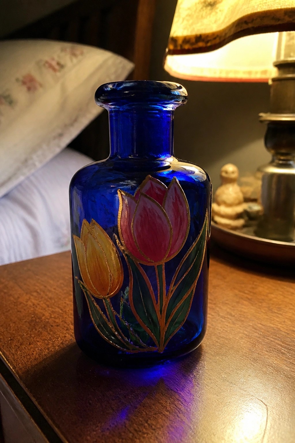 Blue glass bottle with pink and yellow tulip painting on wooden table