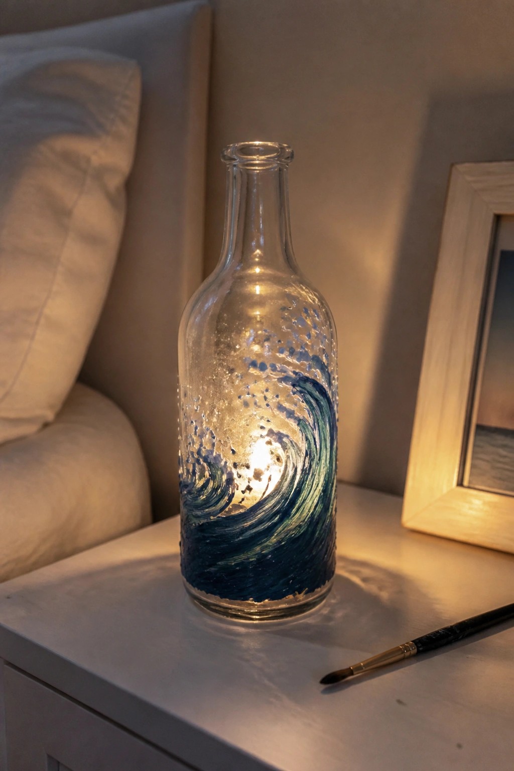Glowing glass bottle with blue wave painting beside paintbrush on nightstand