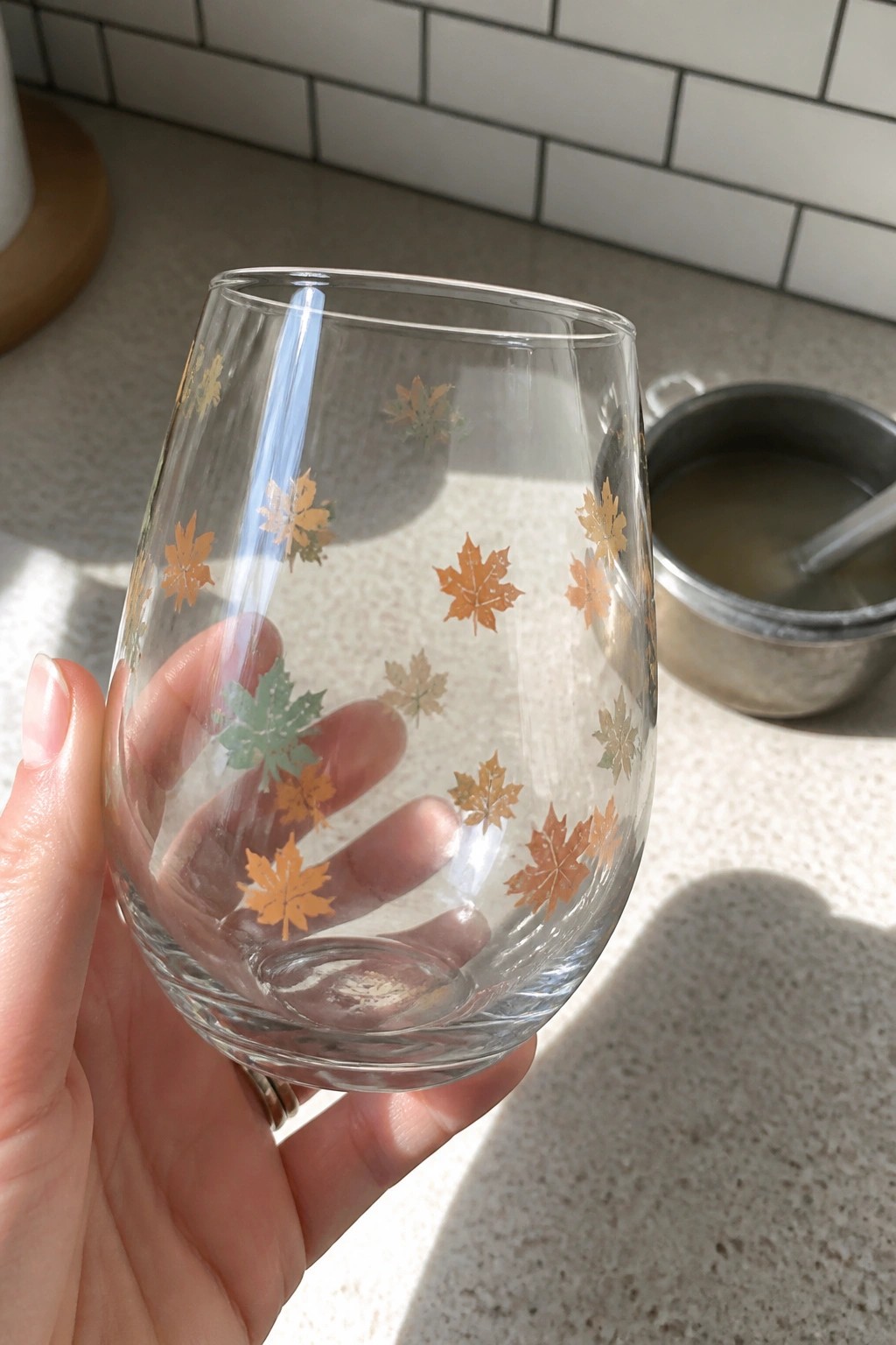 Hand holding stemless glass with gold and green maple leaf decals.