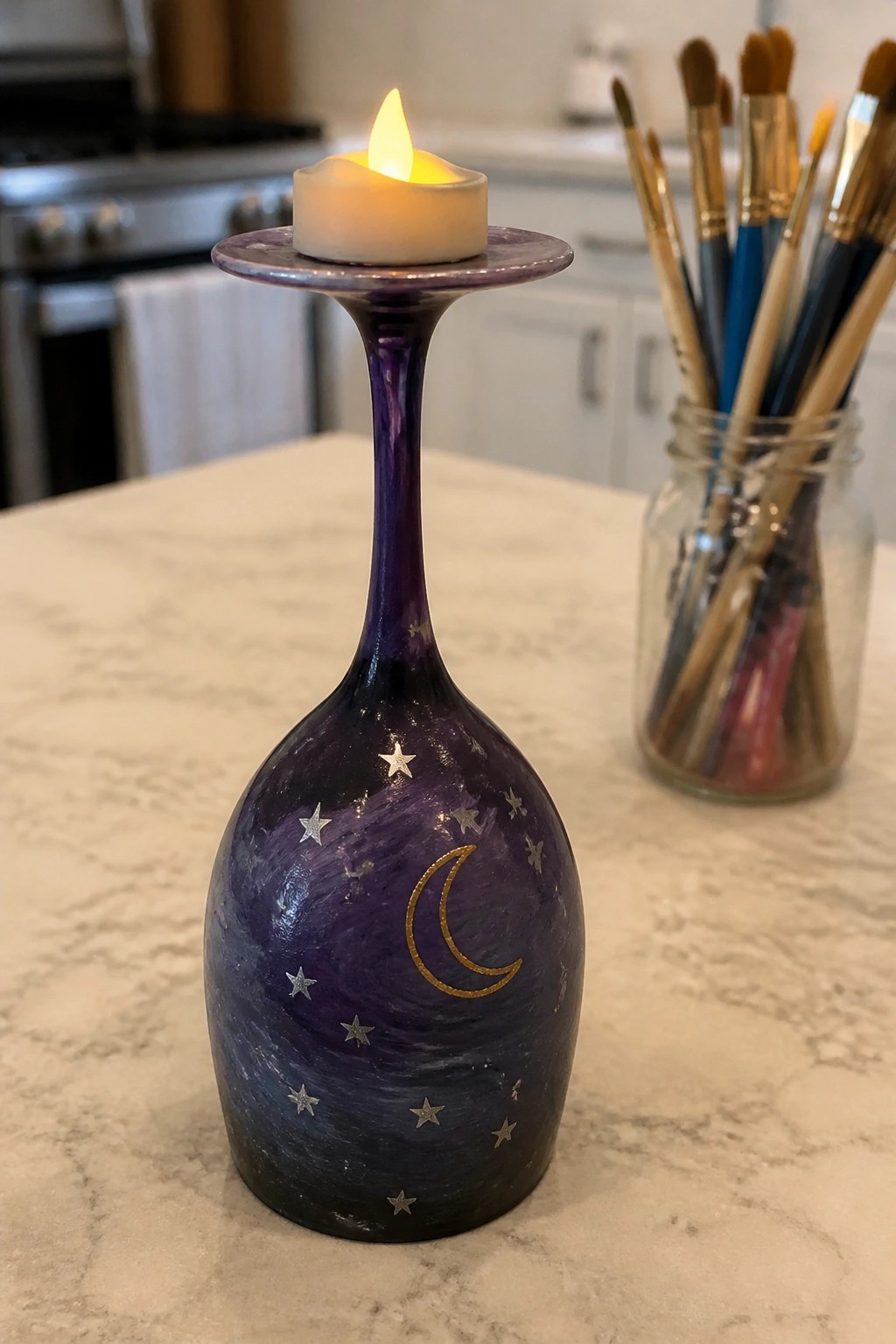 Lit candle on purple wine bottle holder with gold moon and silver stars on marble counter