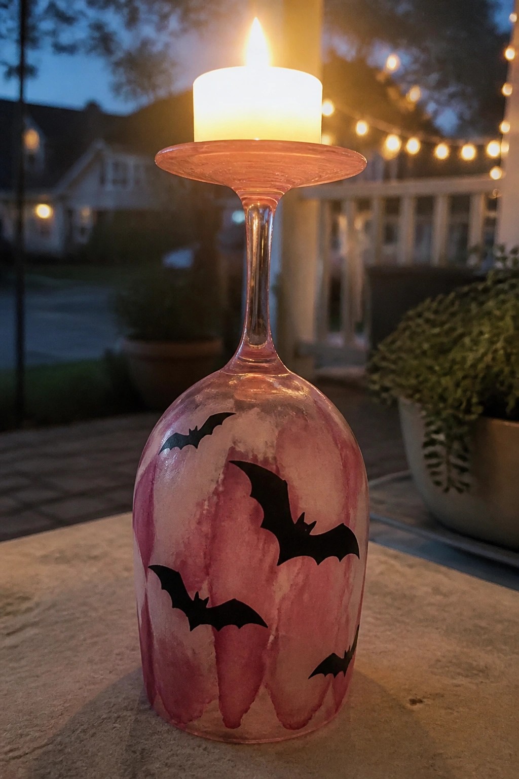 Lit candle on inverted pink wine glass with black bat silhouettes at dusk