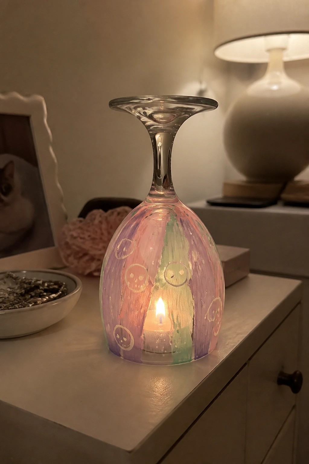Colorful painted wine glass with faces enclosing a glowing lit candle.