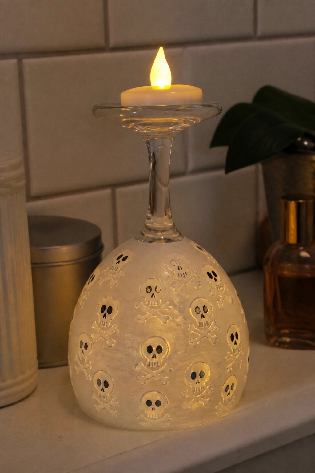 Upside-down frosted wine glass etched with skulls holding a lit candle