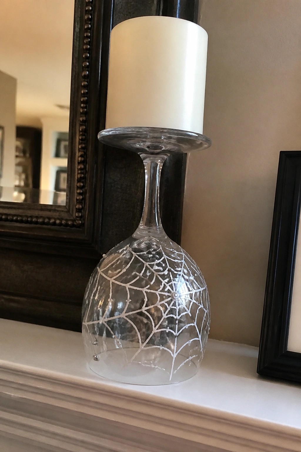 White pillar candle in upside-down spiderweb wine glass on white mantel