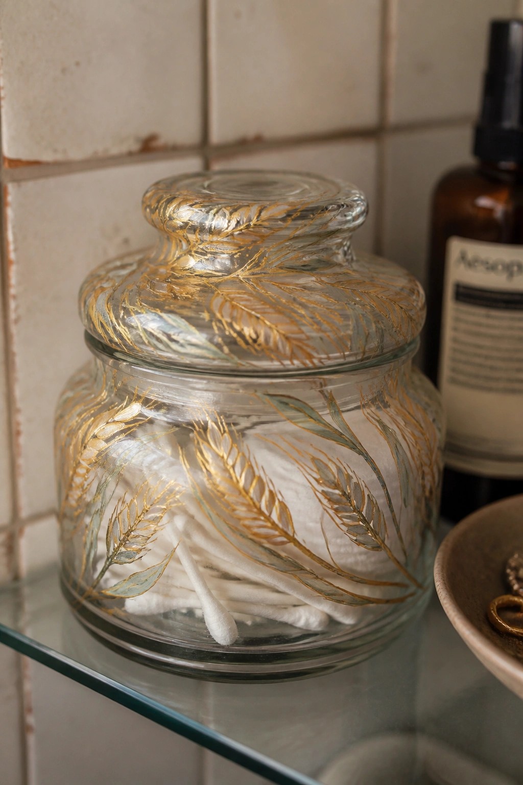 Glass jar with gold leaf patterns holding cotton pads and swabs on shelf