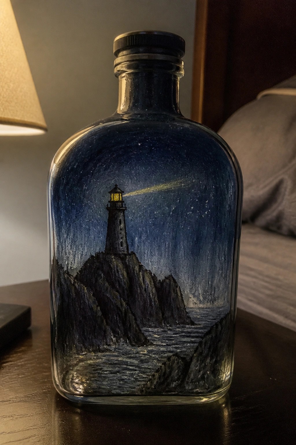 Clear glass bottle with black cap showing a painted lighthouse on dark cliffs at night with ocean waves and a light beam.