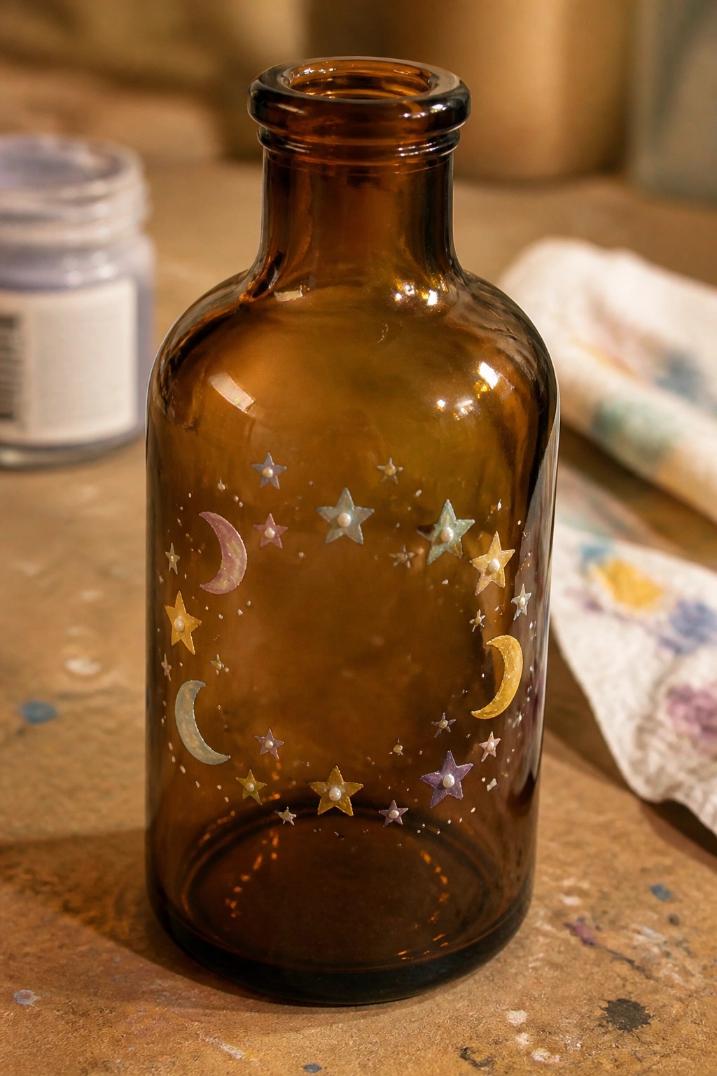 Amber bottle decorated with colorful moons, stars, and pearl accents on wood