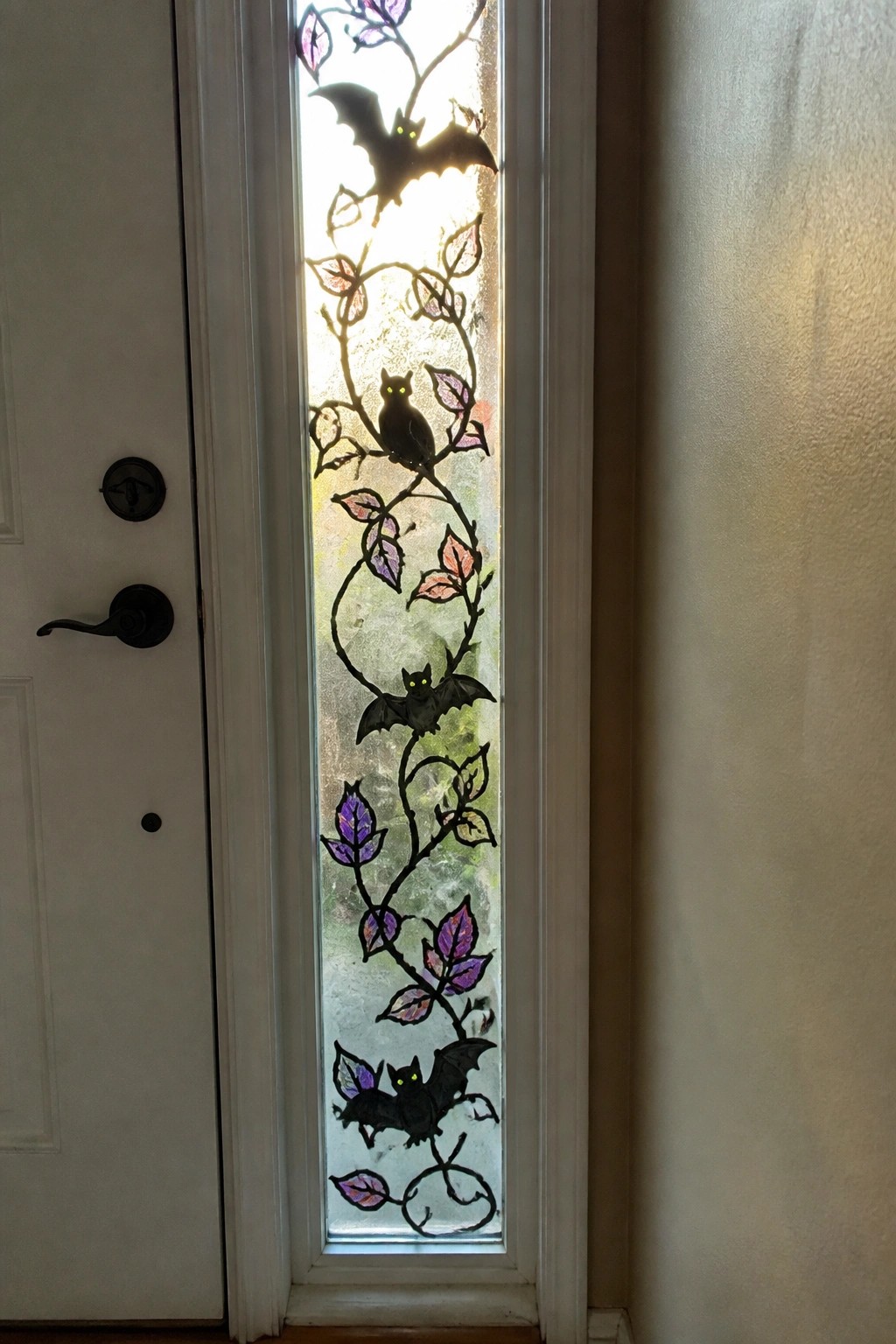 Stained glass door panel with black bats, yellow-eyed cat, and purple leaf vines