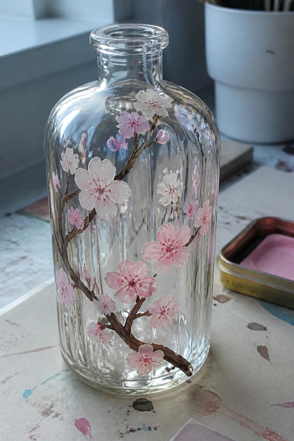 Hand-painted glass bottle with pink cherry blossoms on a splattered table.