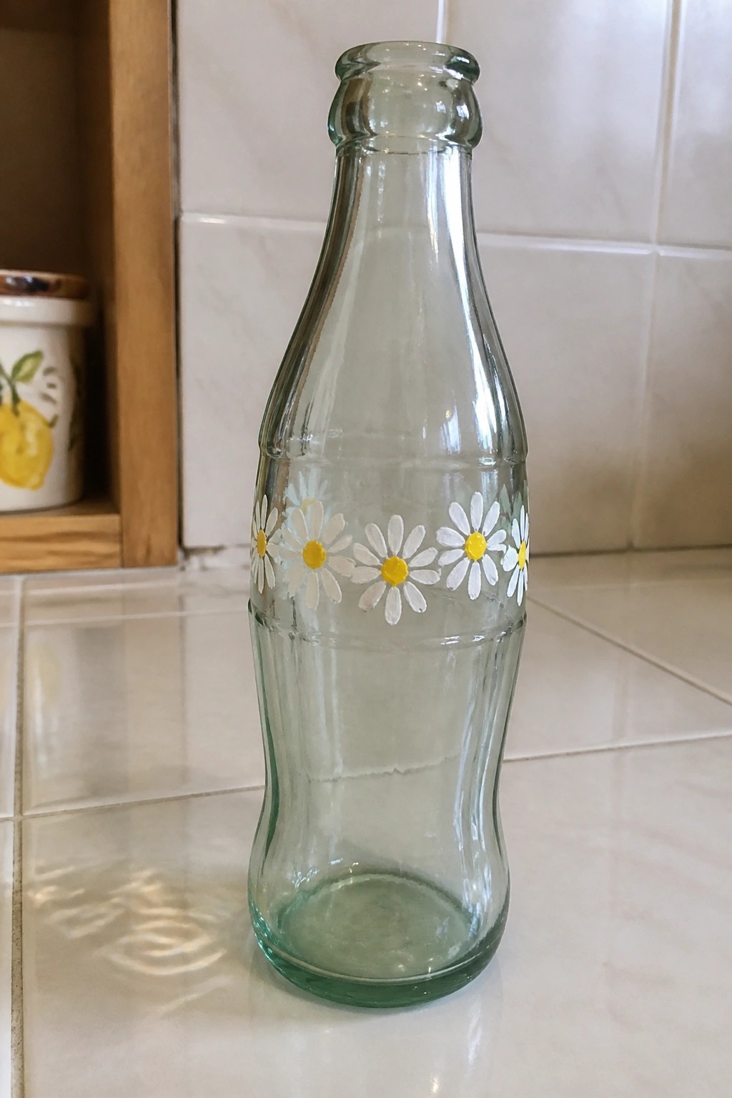 Glass bottle with white and yellow daisy paintings on tiled counter