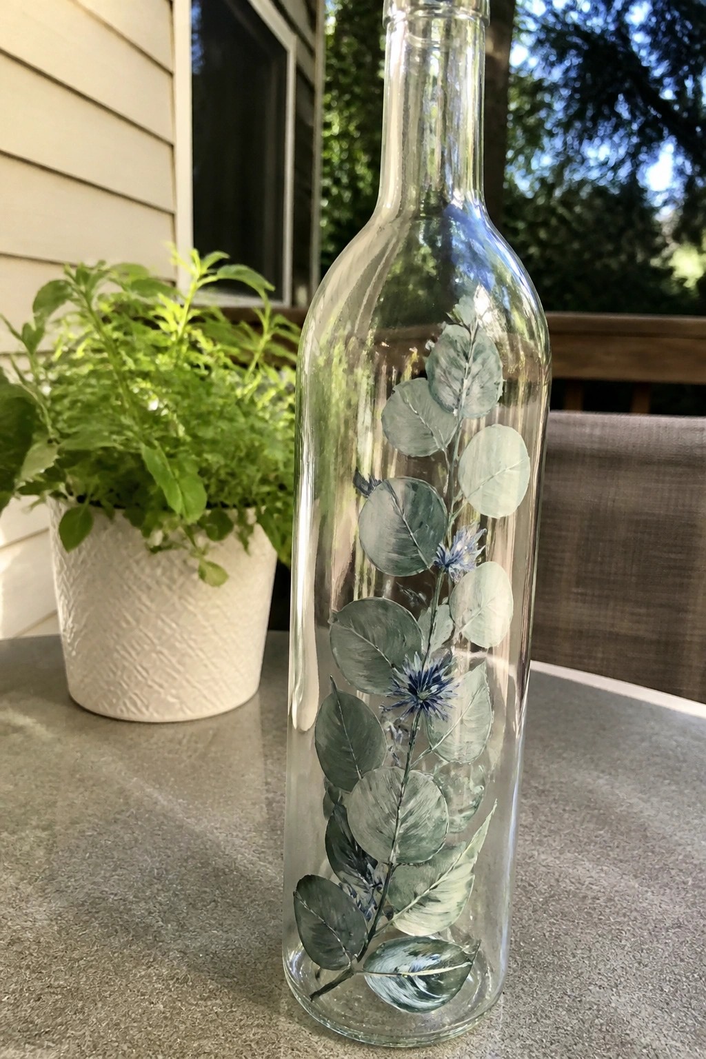 Clear glass bottle painted with green leaves and blue flowers on table