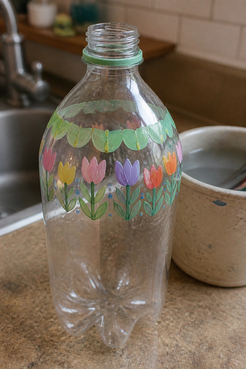 Clear plastic bottle hand-painted with colorful tulips and green scalloped band on kitchen counter