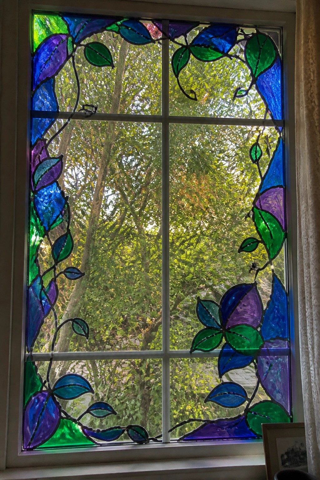 Stained glass window with colorful blue green purple vine and leaf designs framing trees