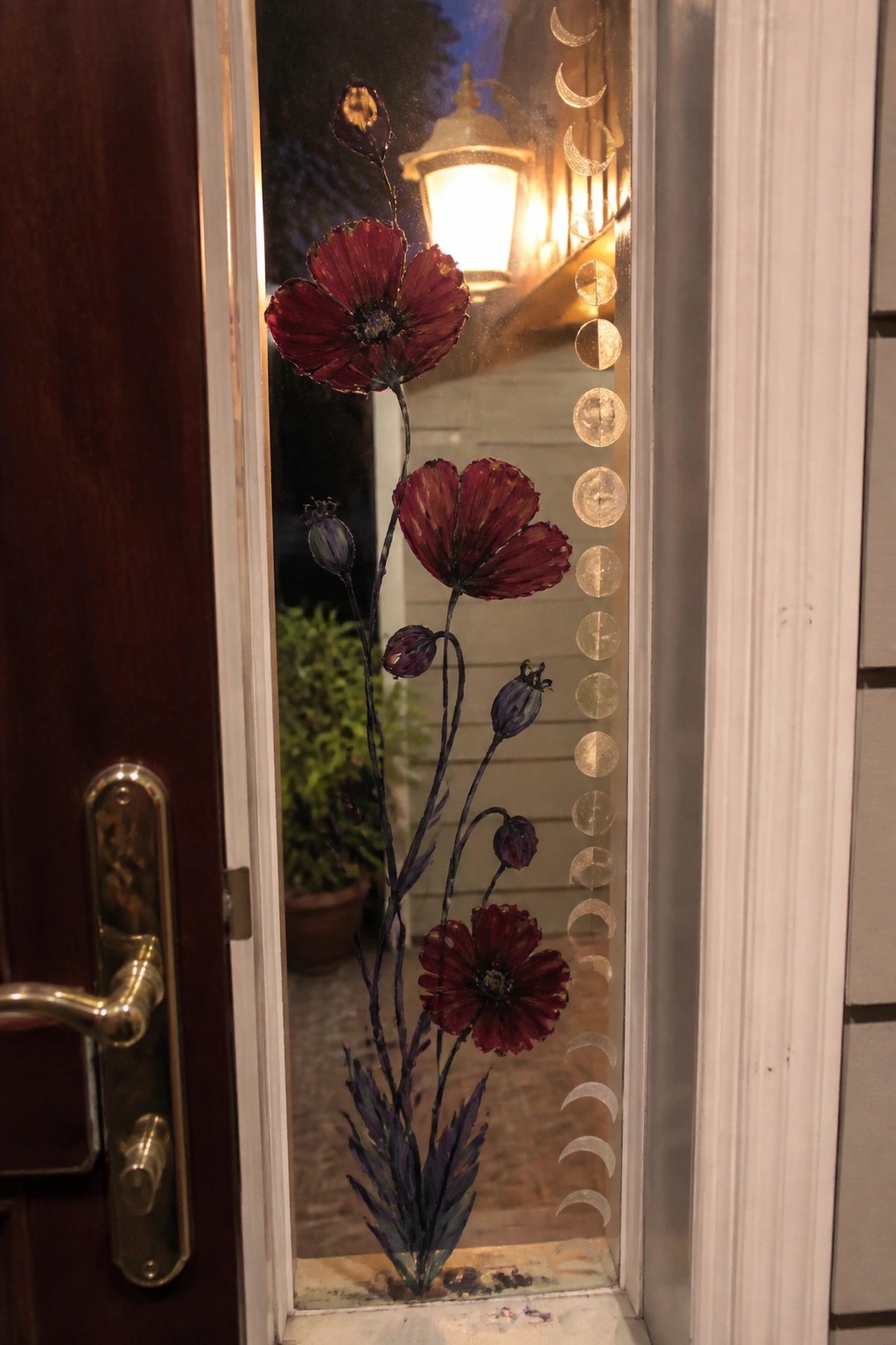 Stained glass door panel with red poppies and moon phase designs at night