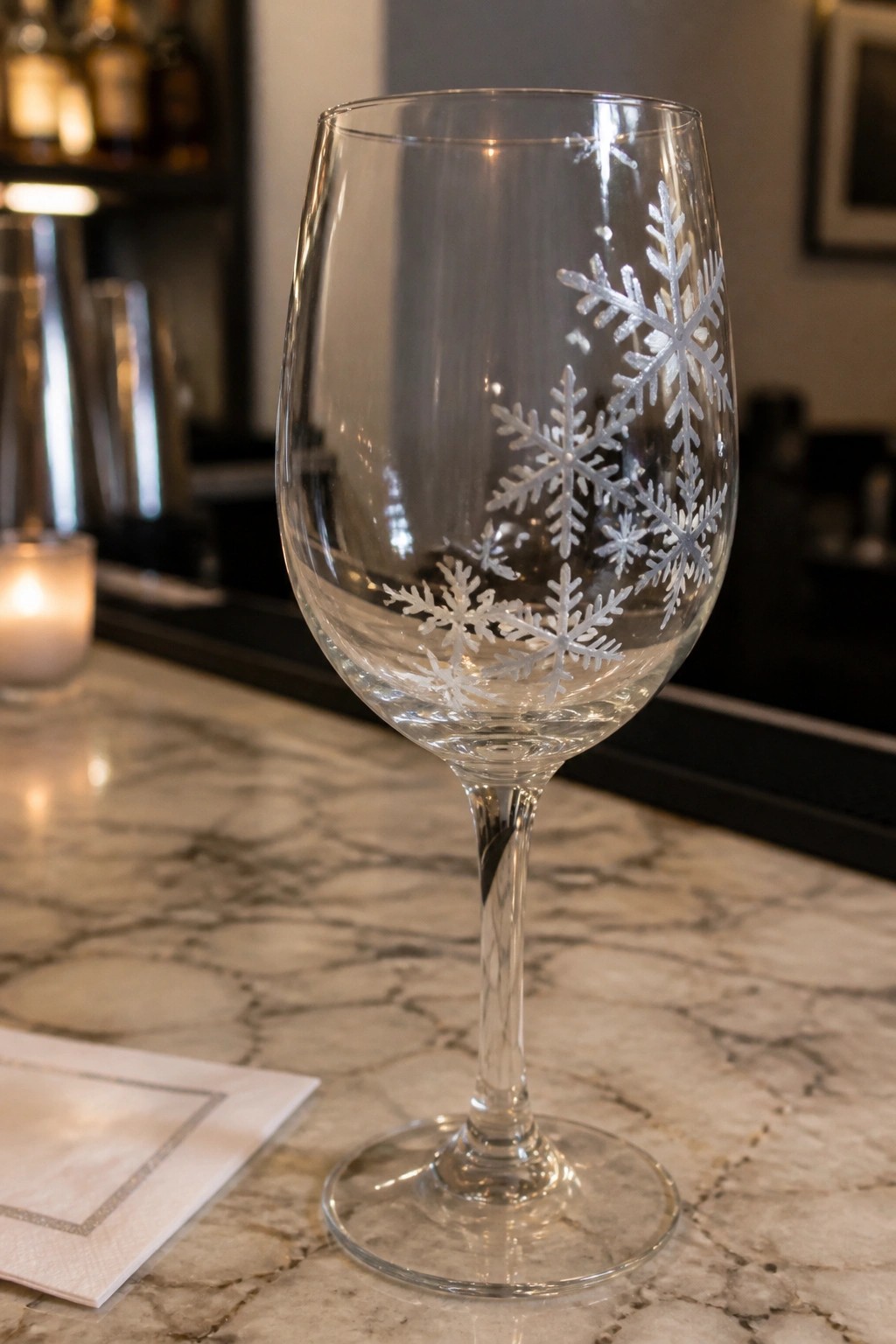 Stemmed wine glass with snowflake etchings on marble countertop near candle