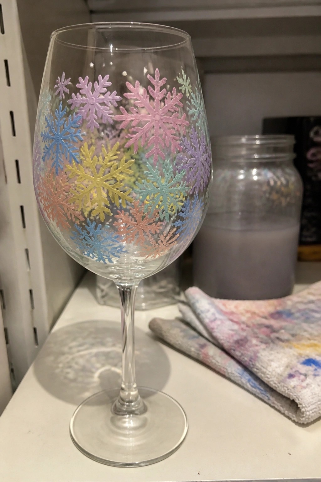 A clear wine glass with clusters of pastel snowflakes painted around the bowl.