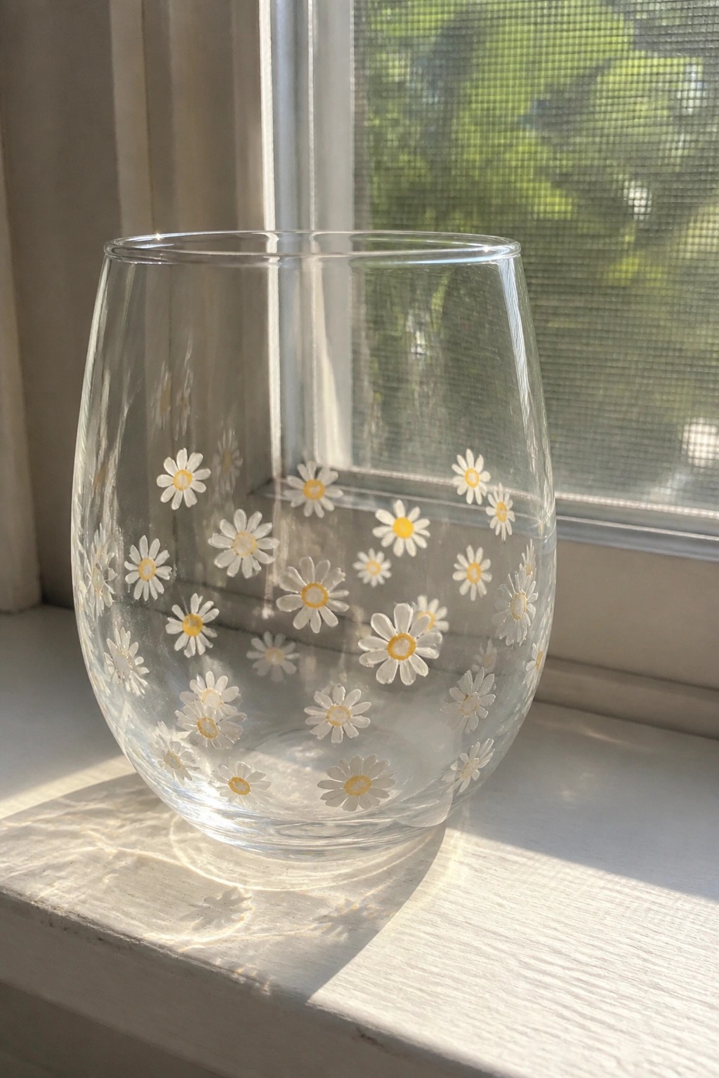 Clear glass tumbler with white and yellow daisies on sunny windowsill