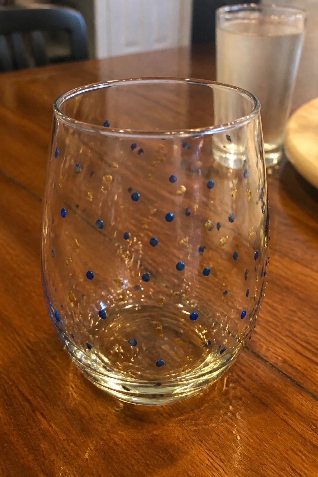 Clear glass tumbler with blue dots and gold flecks on wooden table