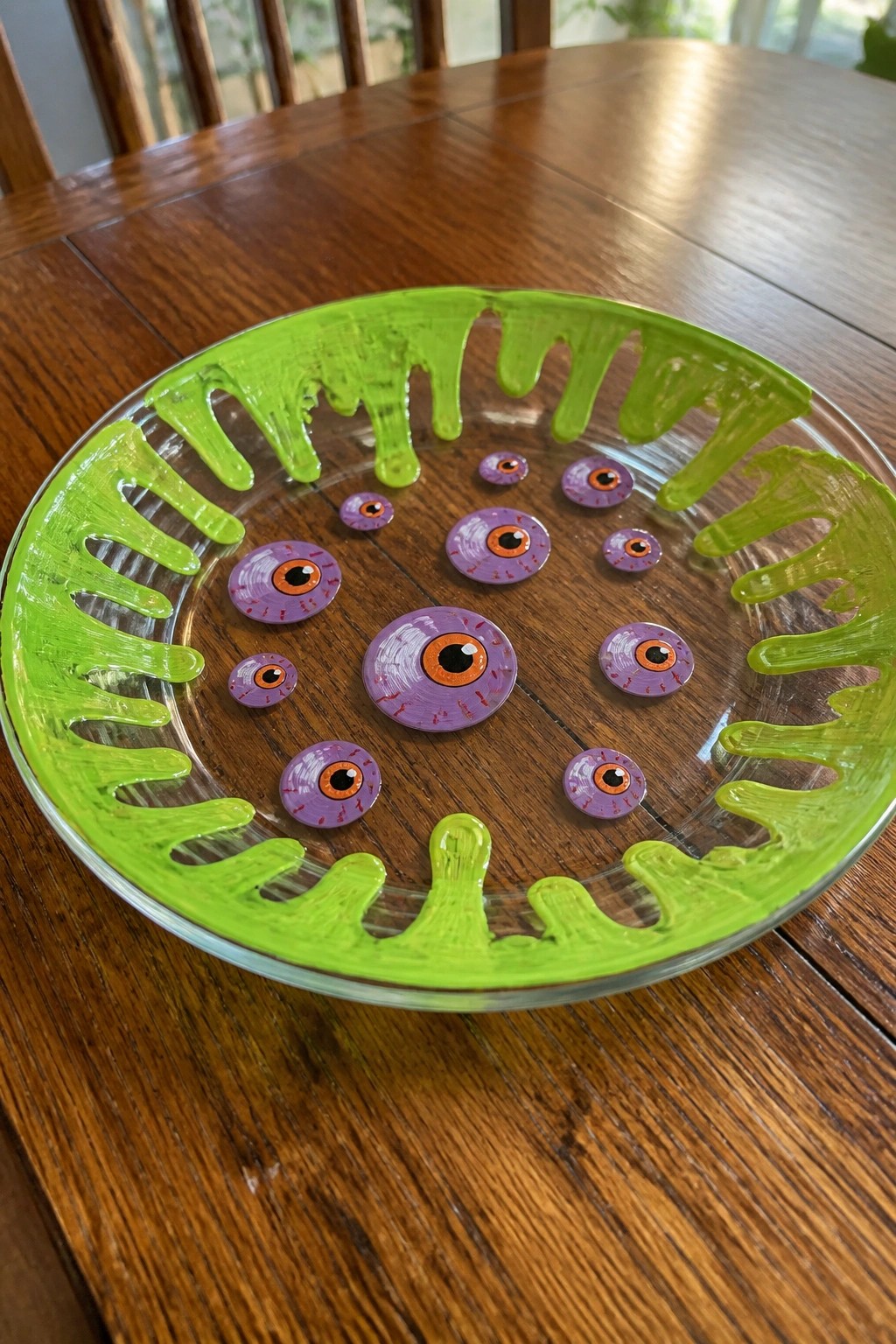 Glass plate with dripping green rim and scattered purple monster eyeballs on wood table