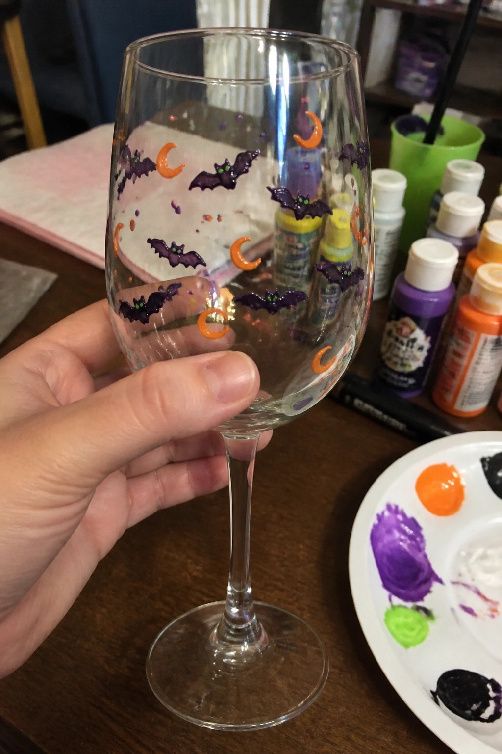 Hand holding wine glass painted with purple bats and orange moons.