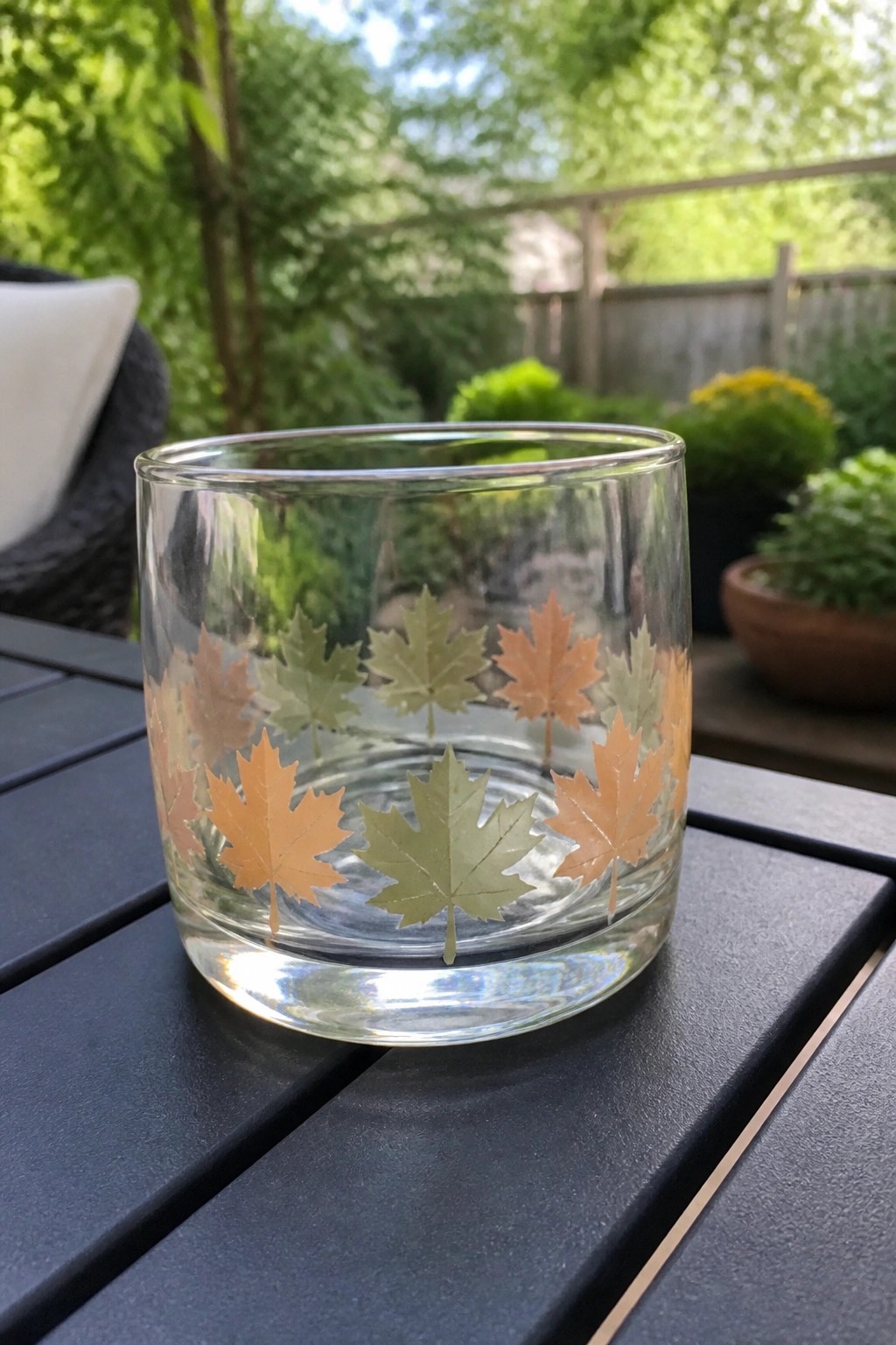 Clear glass tumbler with orange and green maple leaf designs on dark outdoor table