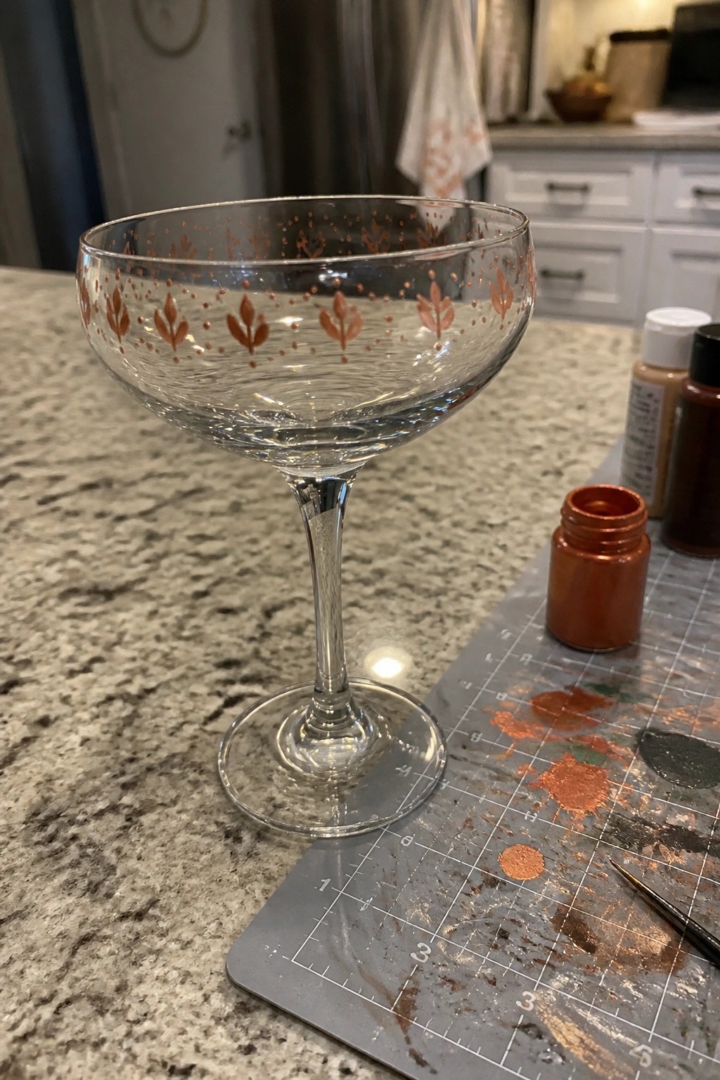 Coupe glass with copper leaf designs beside open paint jar on marble counter
