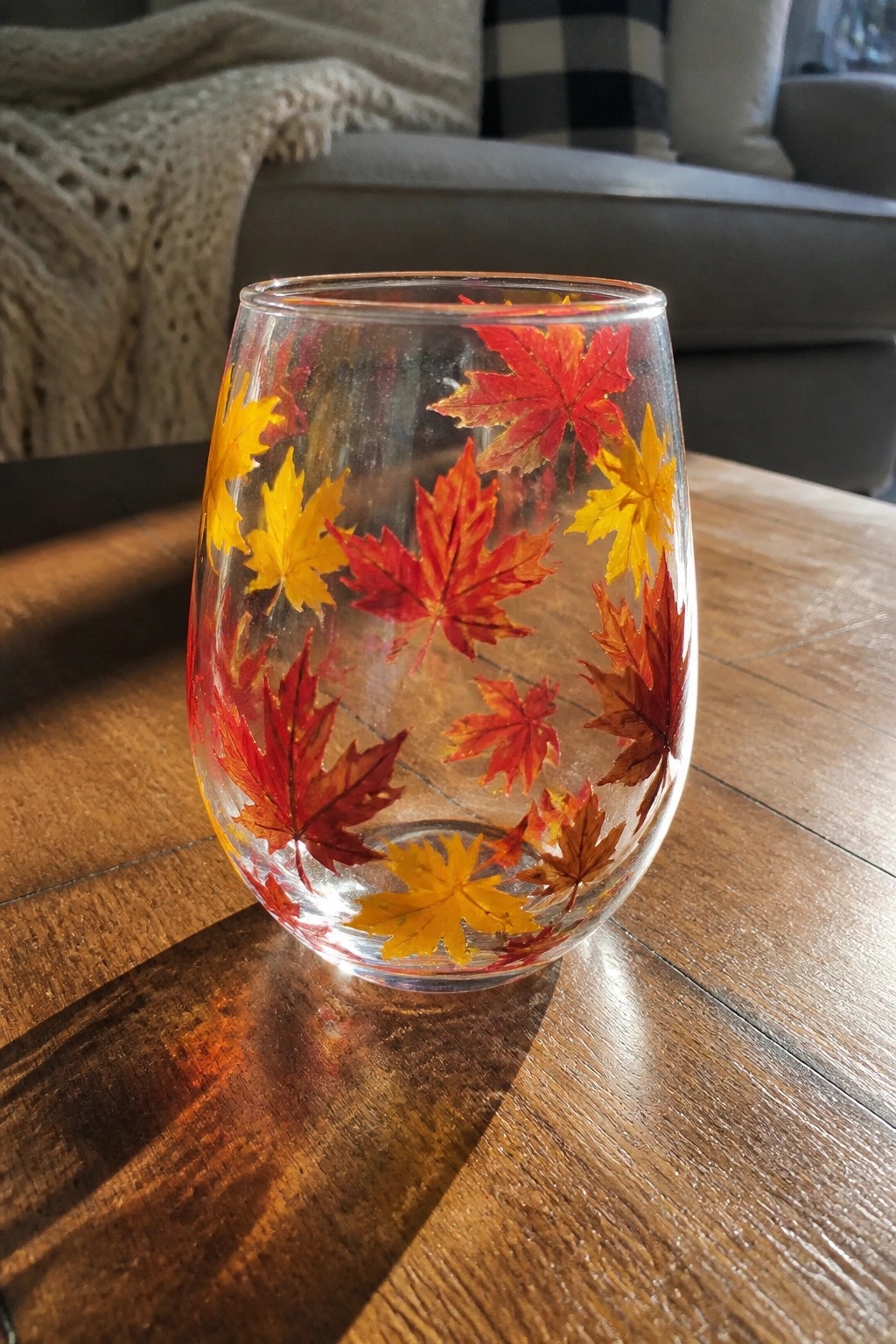 Clear stemless glass with red, orange, and yellow maple leaves on wooden table