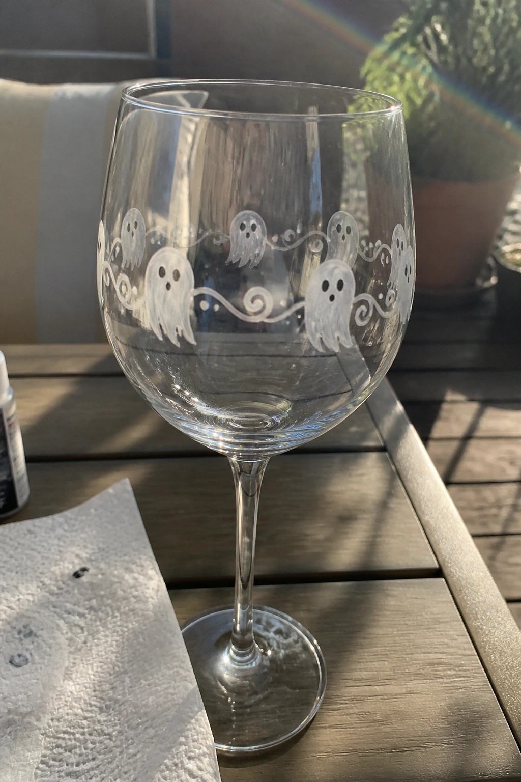 Clear wine glass with white ghost and swirl designs on wooden patio table