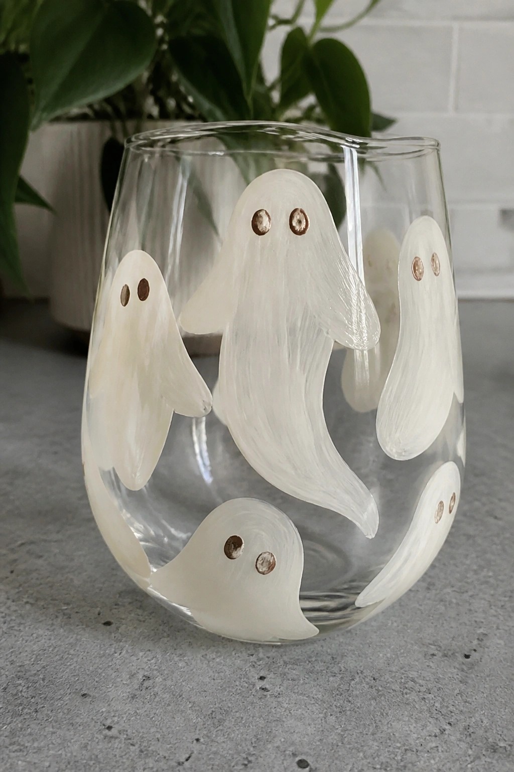 Clear stemless glass with white ghost figures and metallic copper eyes near plant.