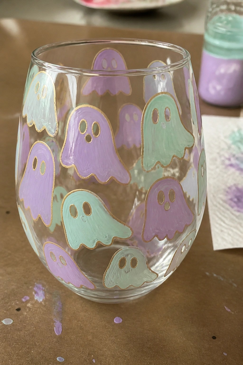 Stemless glass tumbler hand-painted with pastel purple, mint, and blue ghosts outlined in gold.