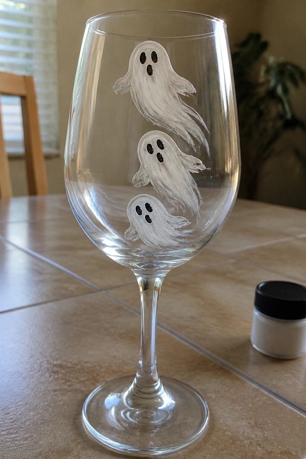 Wine glass with three stacked white ghosts painted beside small jar on table