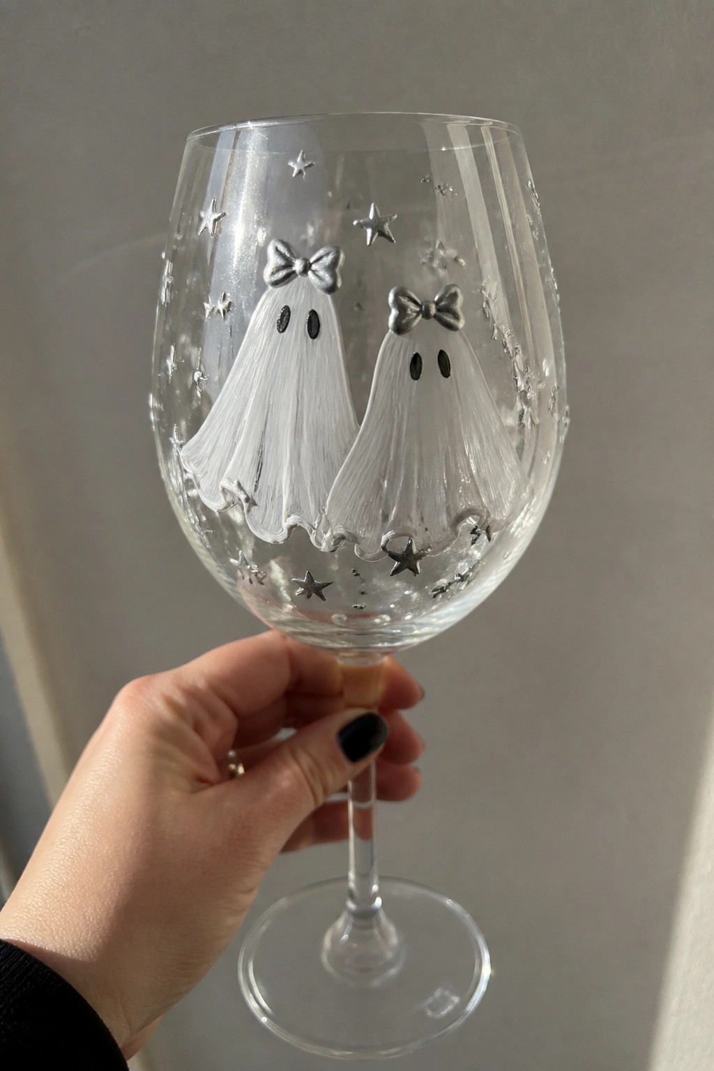 Hand holding wine glass with two ghost figures, bows, and silver stars