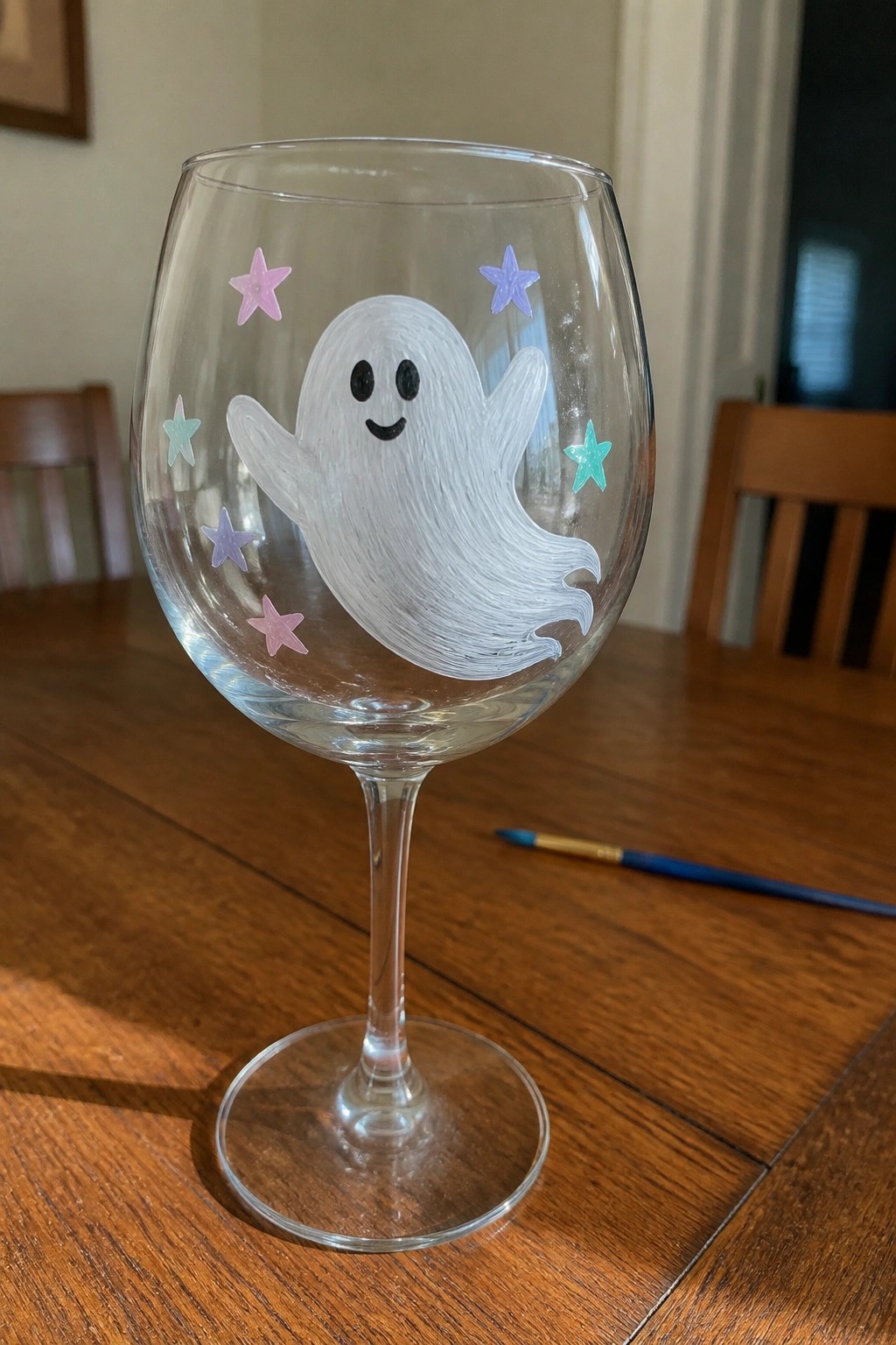 Wine glass with painted white ghost and colorful stars on wooden table